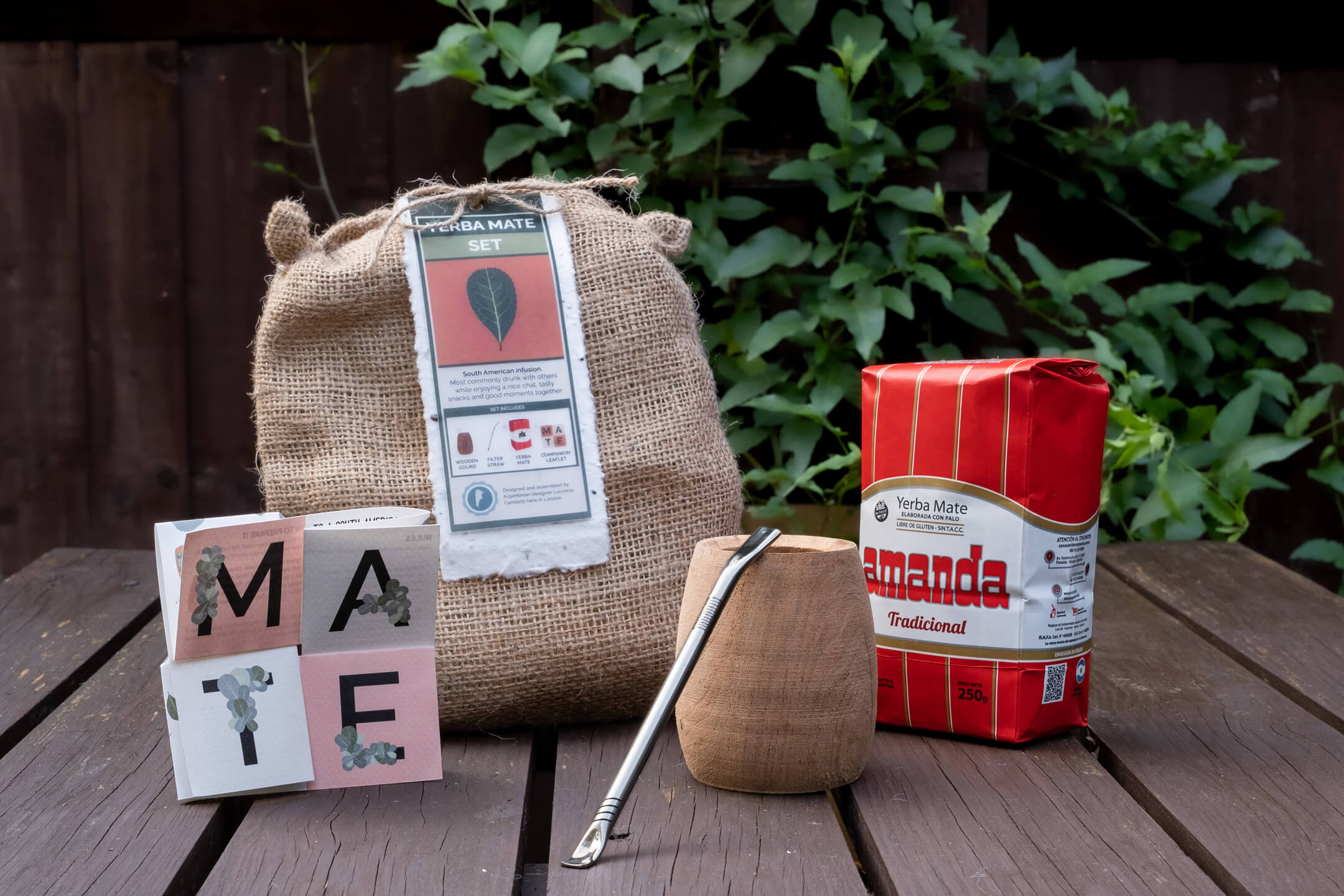 A wooden mate gourd with a metal straw, beside the Yerba Mate Set's companion leaflet and a bag of yerba mate